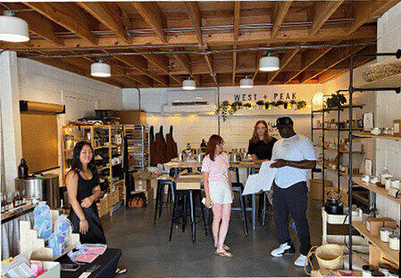 Shoppers and staff inside the West + Peak candle studio at The Webb, with shelves of candles and a wood-beamed ceiling