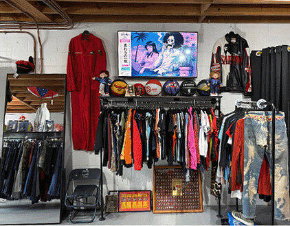 Inside Seams Right: racks of vintage clothing, a red coverall, a wall TV and bleached denim under a wood-beamed ceiling