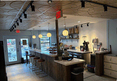 Inside V’s Coffee Collab: a long wood coffee bar with stools, pendant lights and a pressed-tin ceiling